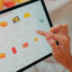 Imagem de uma tela de tablet com um dedo apontando para os produtos mostrados nele