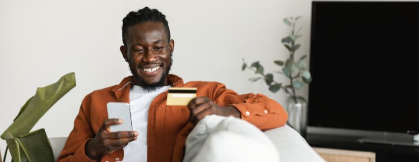 Homem sentado no sofá com cartão de crédito na mão e o celular